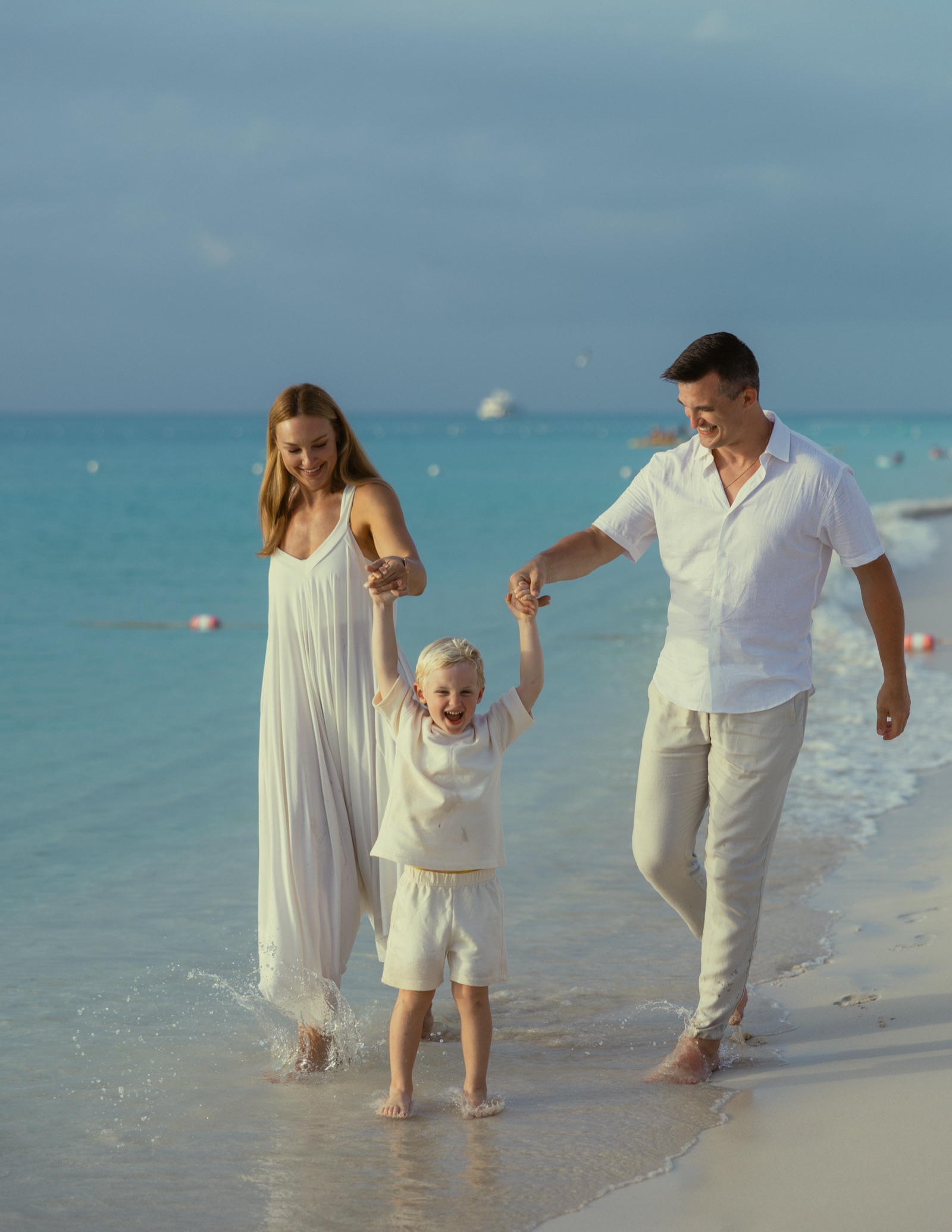 Jon, Jaclyn, and their son walking in the surf on a beach