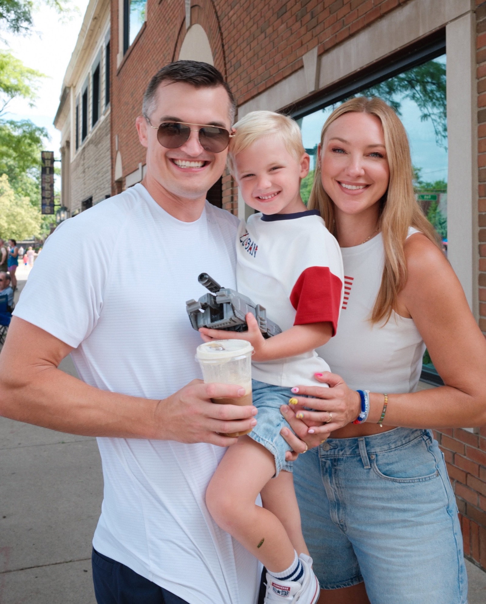 Jon, Jaclyn, and their son downtown with a toy tank and an iced coffee